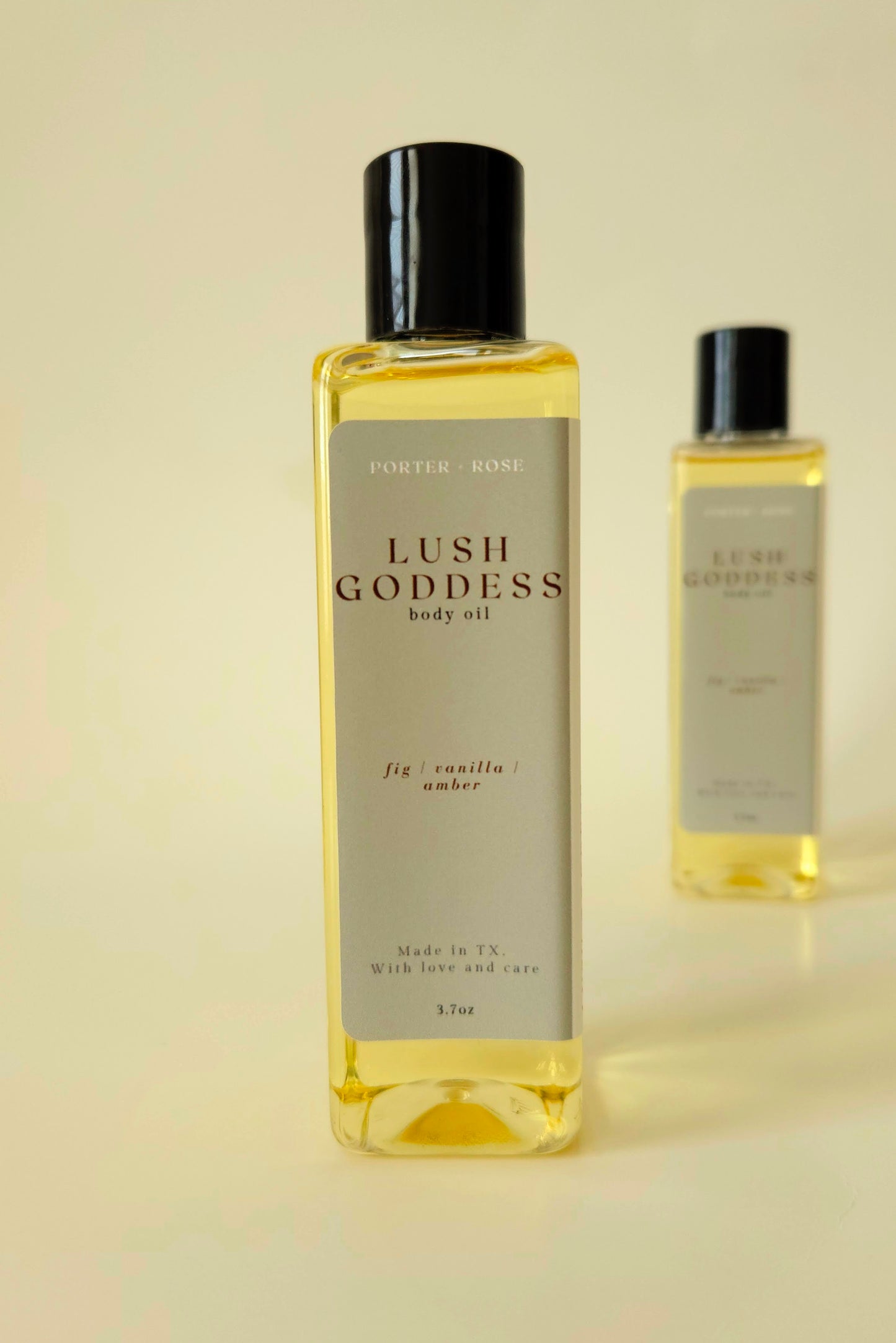 Lush Goddess body oil in a rectangular plastic bottle, styled with fig, honey, and greenery to reflect the scent's earthy, sweet profile.