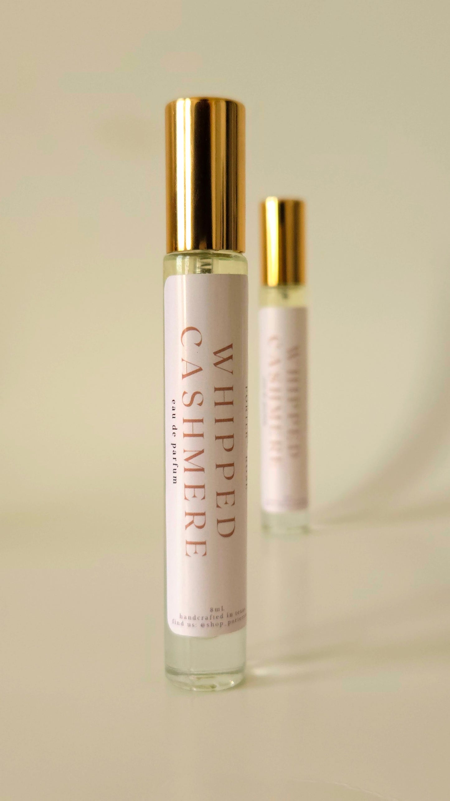 Two 'Whipped Cashmere' perfume bottles on a beige background