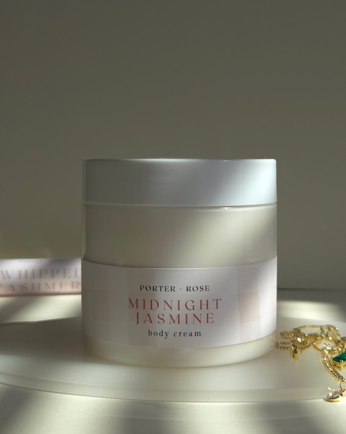 Jar of Porter & Rose Midnight Jasmine body cream on a reflective surface with a soft background