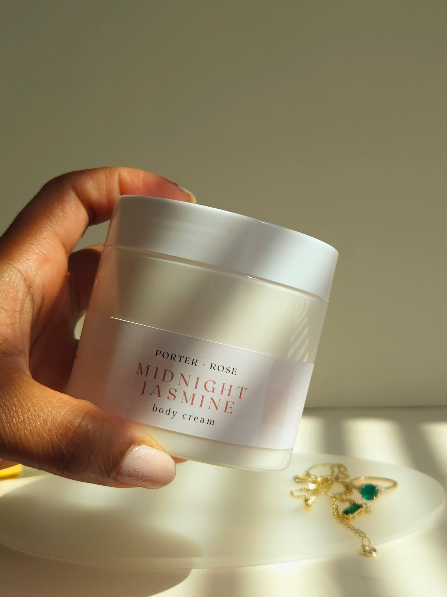 Hand holding a jar of 'Porter & Rose Midnight Jasmine' body cream with a soft background.