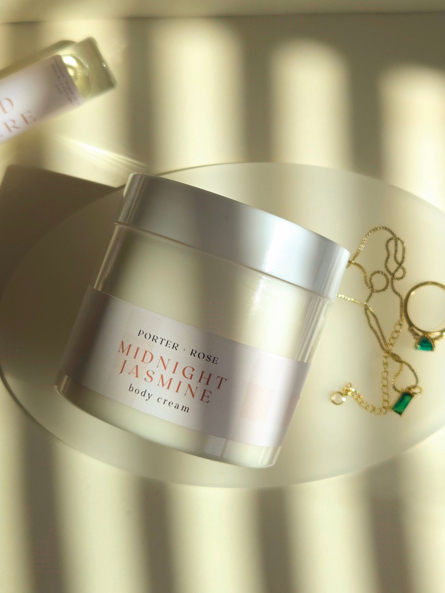 Jar of Porter & Rose Midnight Jasmine body cream on a reflective surface with jewelry in the background