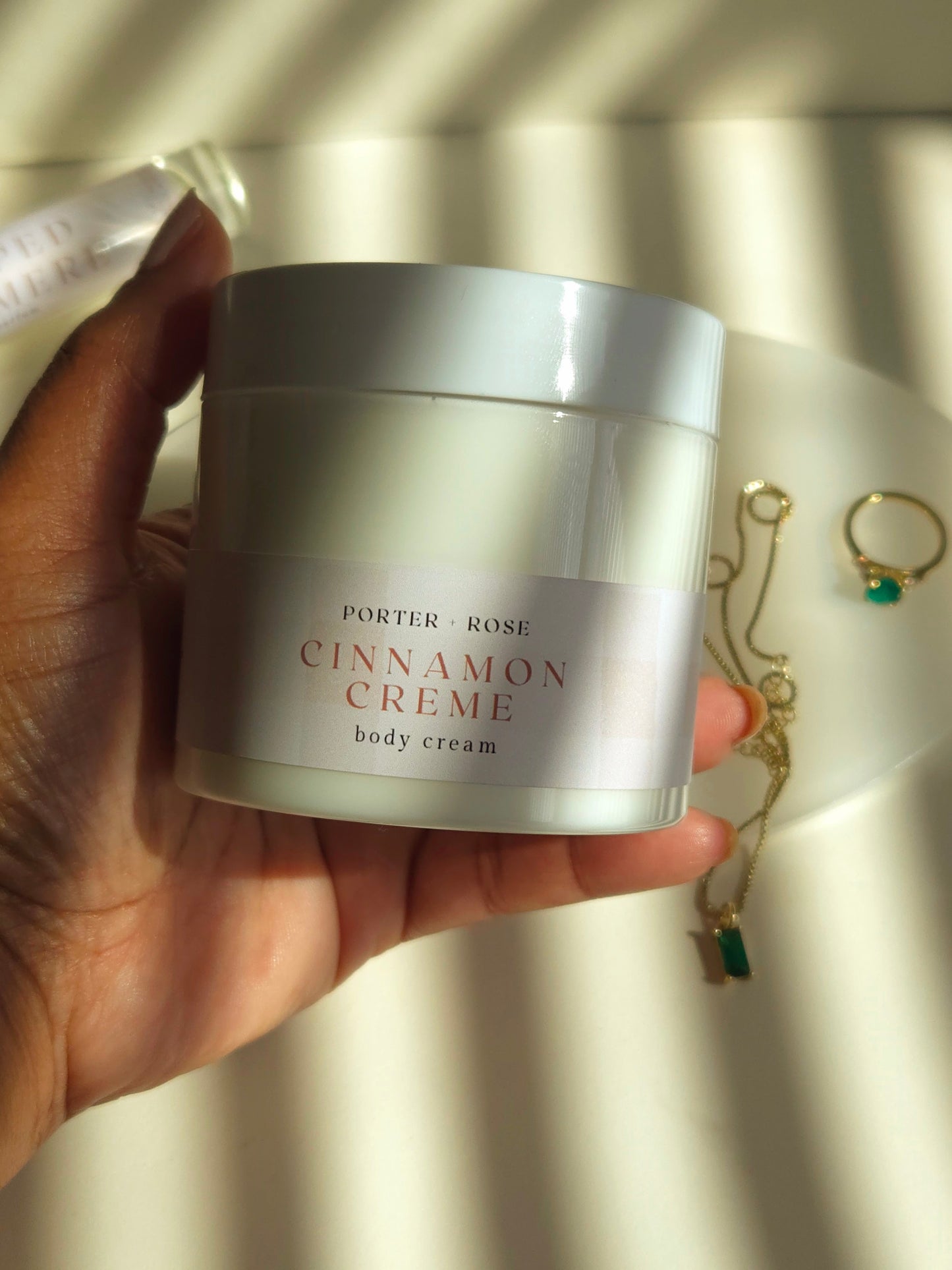 Hand holding a jar of 'Cinnamon Crème' body cream with a blurred background