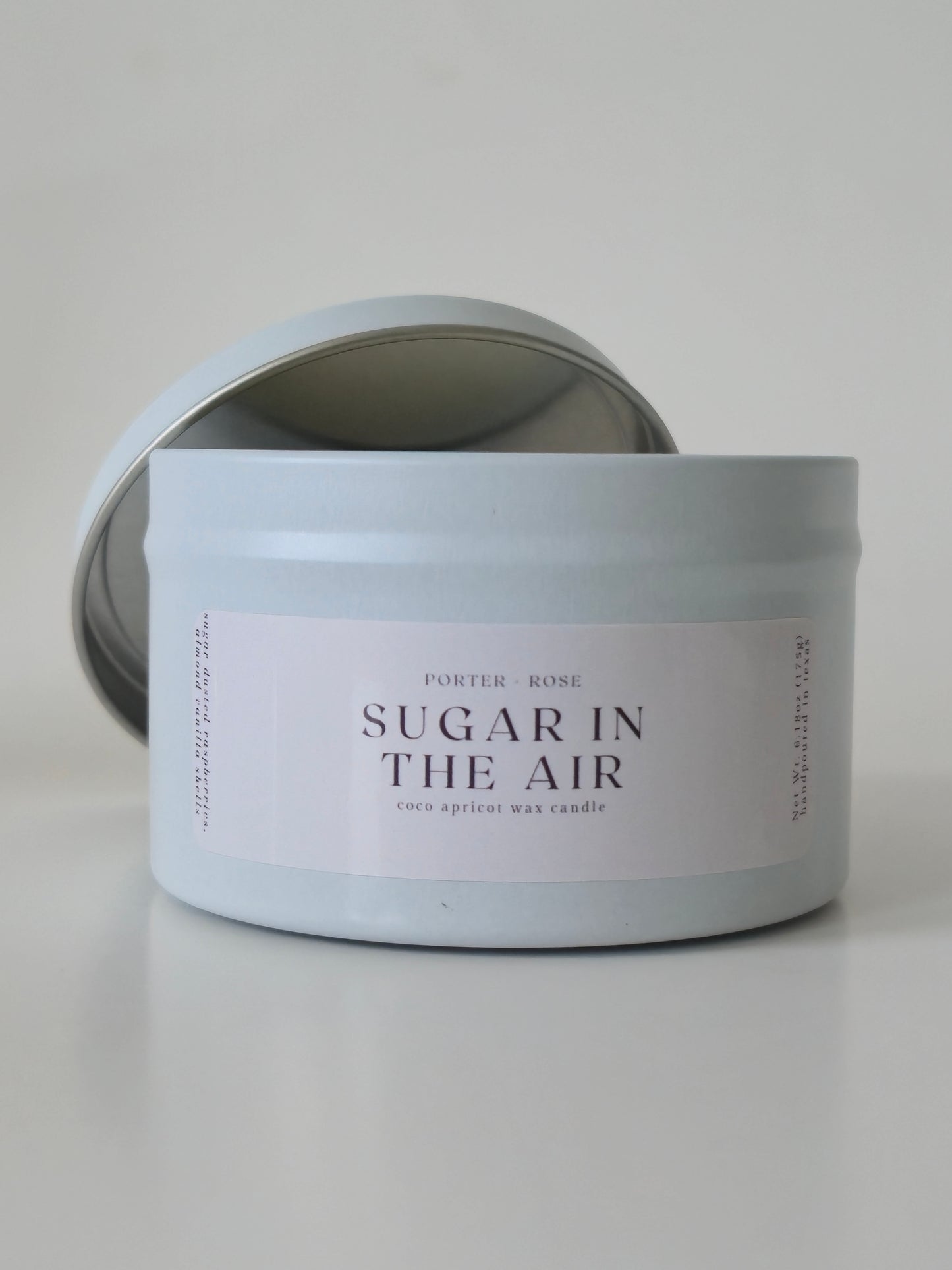 Sugar in the Air a small metal tin scented candle that smells like sweet macarons. White Wooden Wick Candle on a light gray background - porter + rose