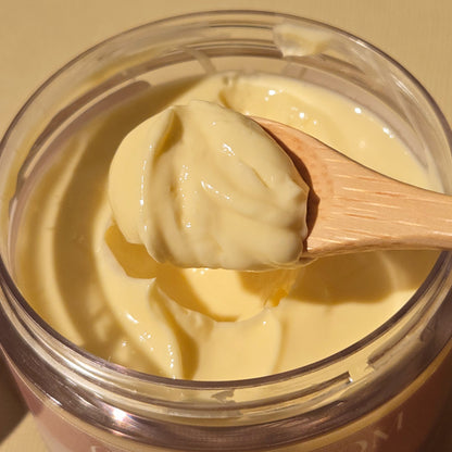 Hands scooping out a creamy, beige body butter from a jar. Rich and moisturizing texture.