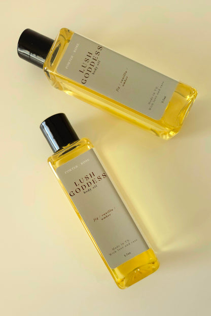 Lush Goddess body oil in a rectangular plastic bottle, styled with fig, honey, and greenery to reflect the scent's earthy, sweet profile.
