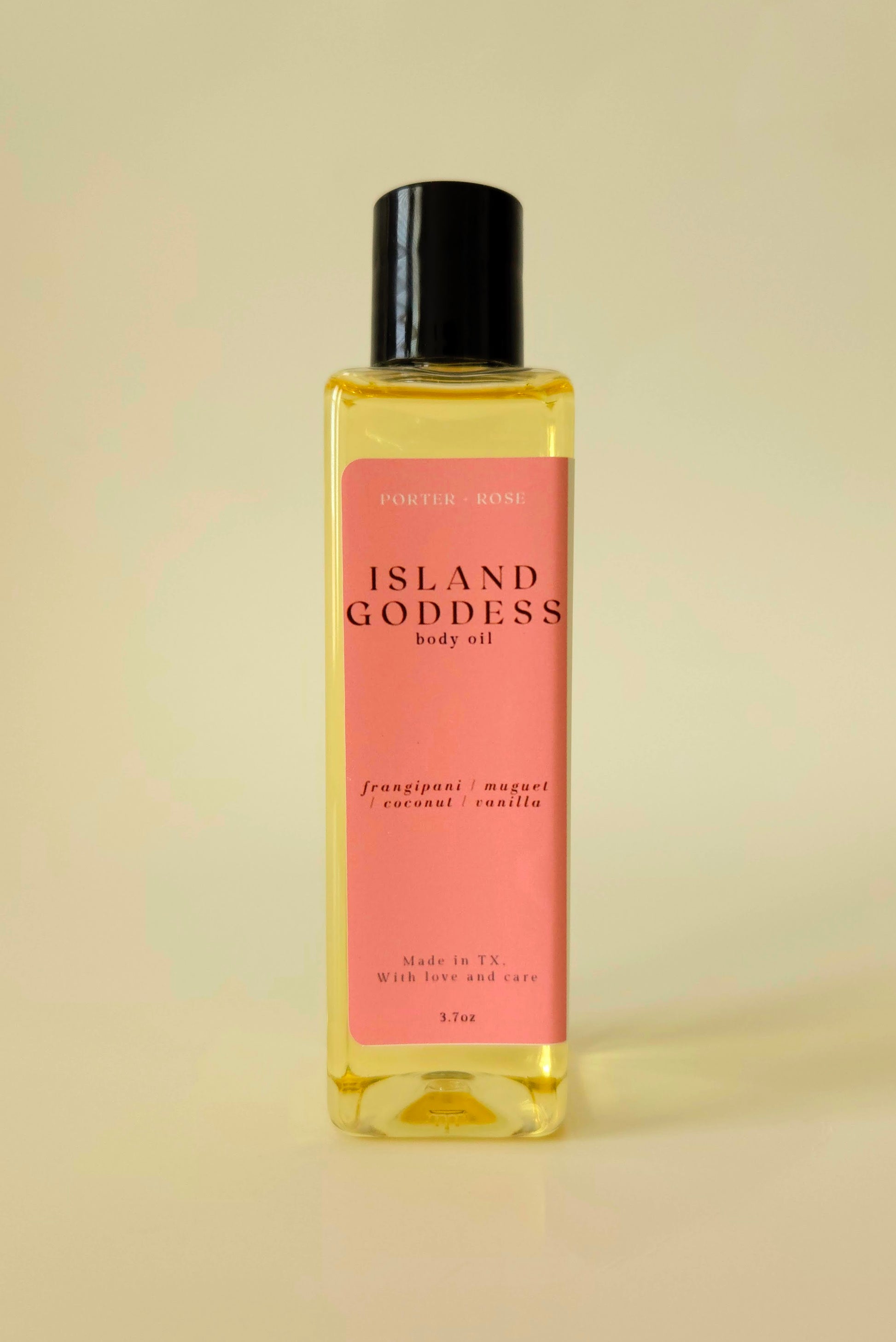 Island Goddess body oil in a clear rectangular bottle, styled with tropical flowers and coconut to reflect its creamy, floral scent.