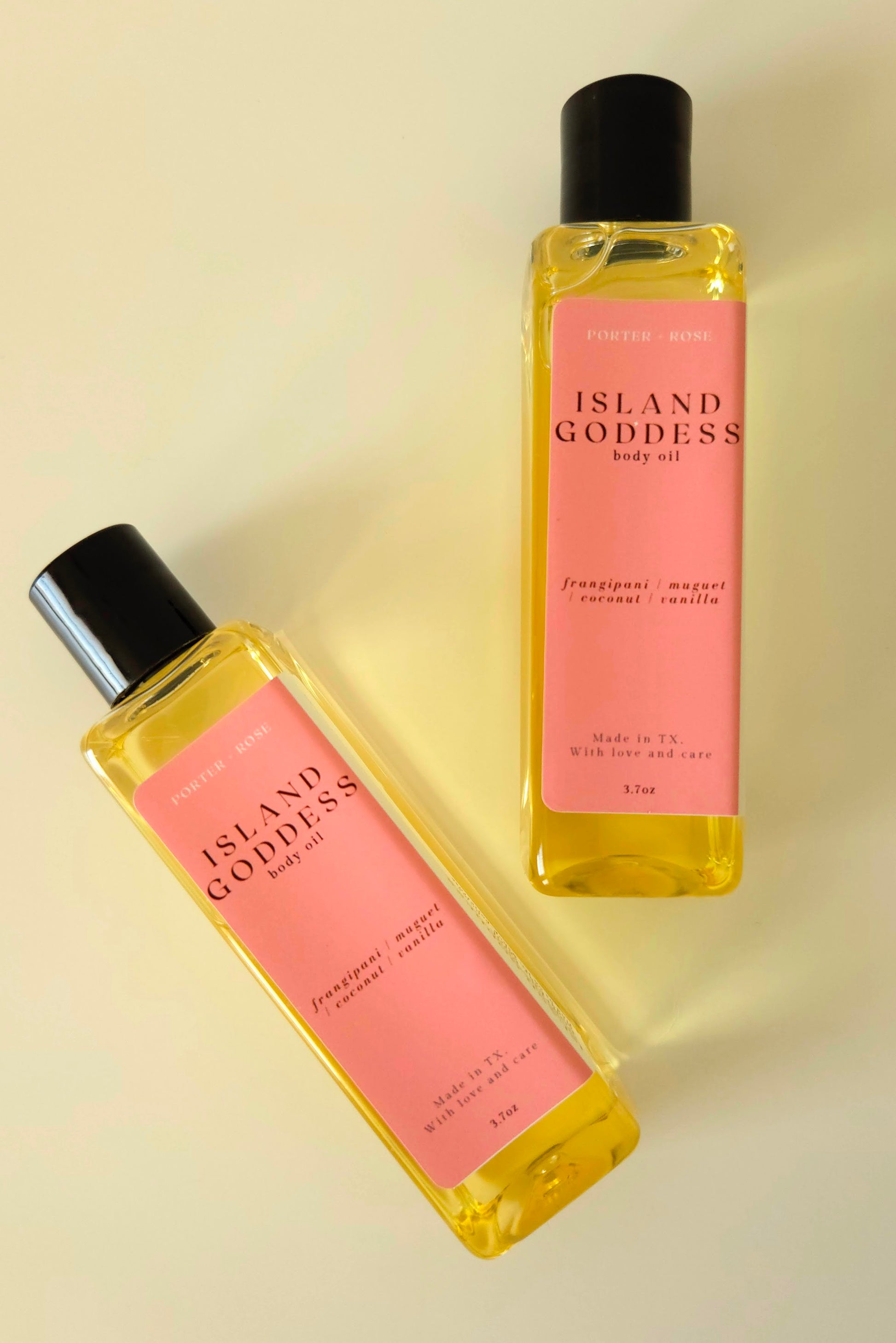 Island Goddess body oil in a clear rectangular bottle, styled with tropical flowers and coconut to reflect its creamy, floral scent.