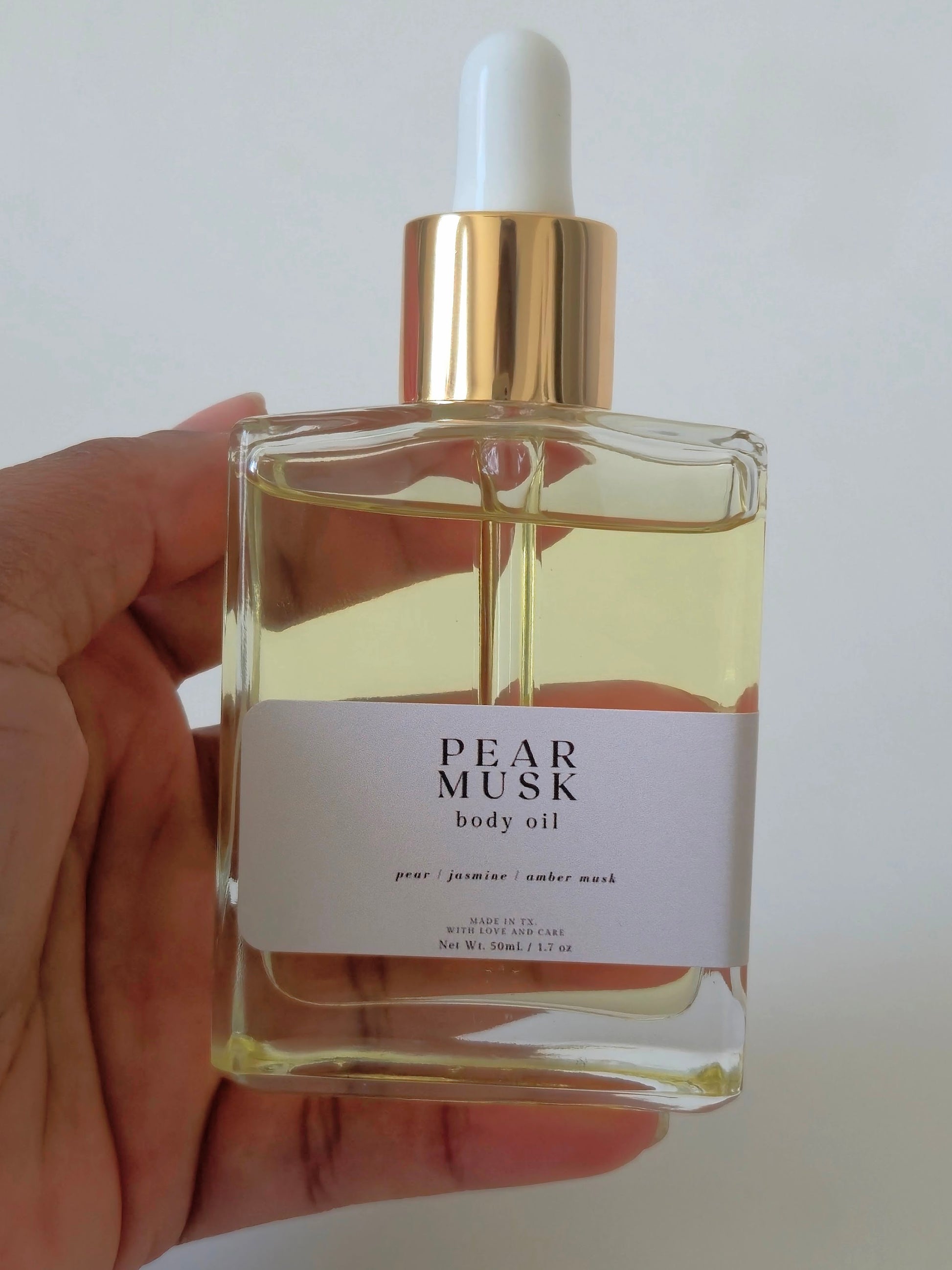 Hand holding a bottle of Pear Musk body oil with a white background