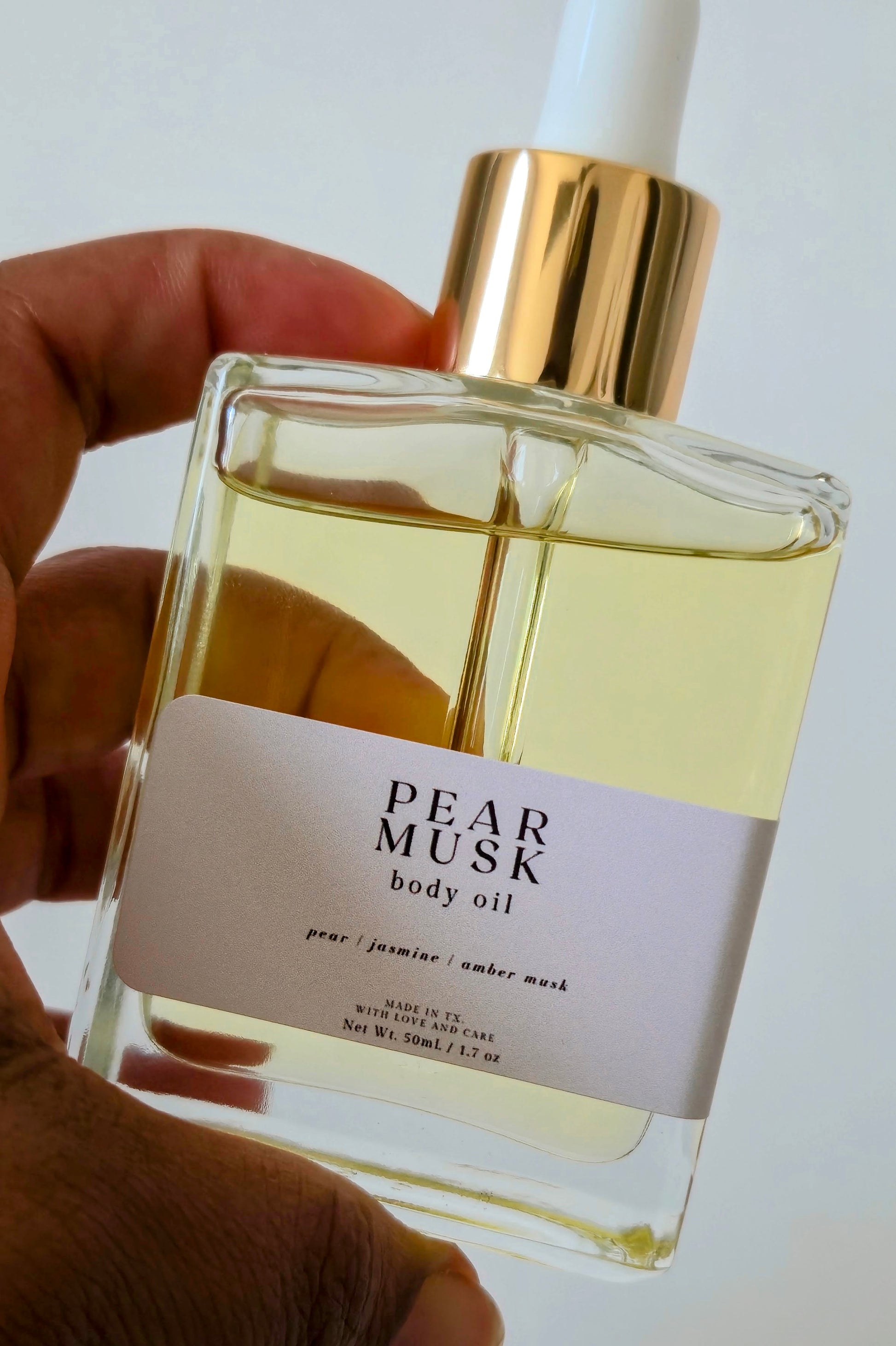 Pear Musk body oil bottle held by a hand with a white background