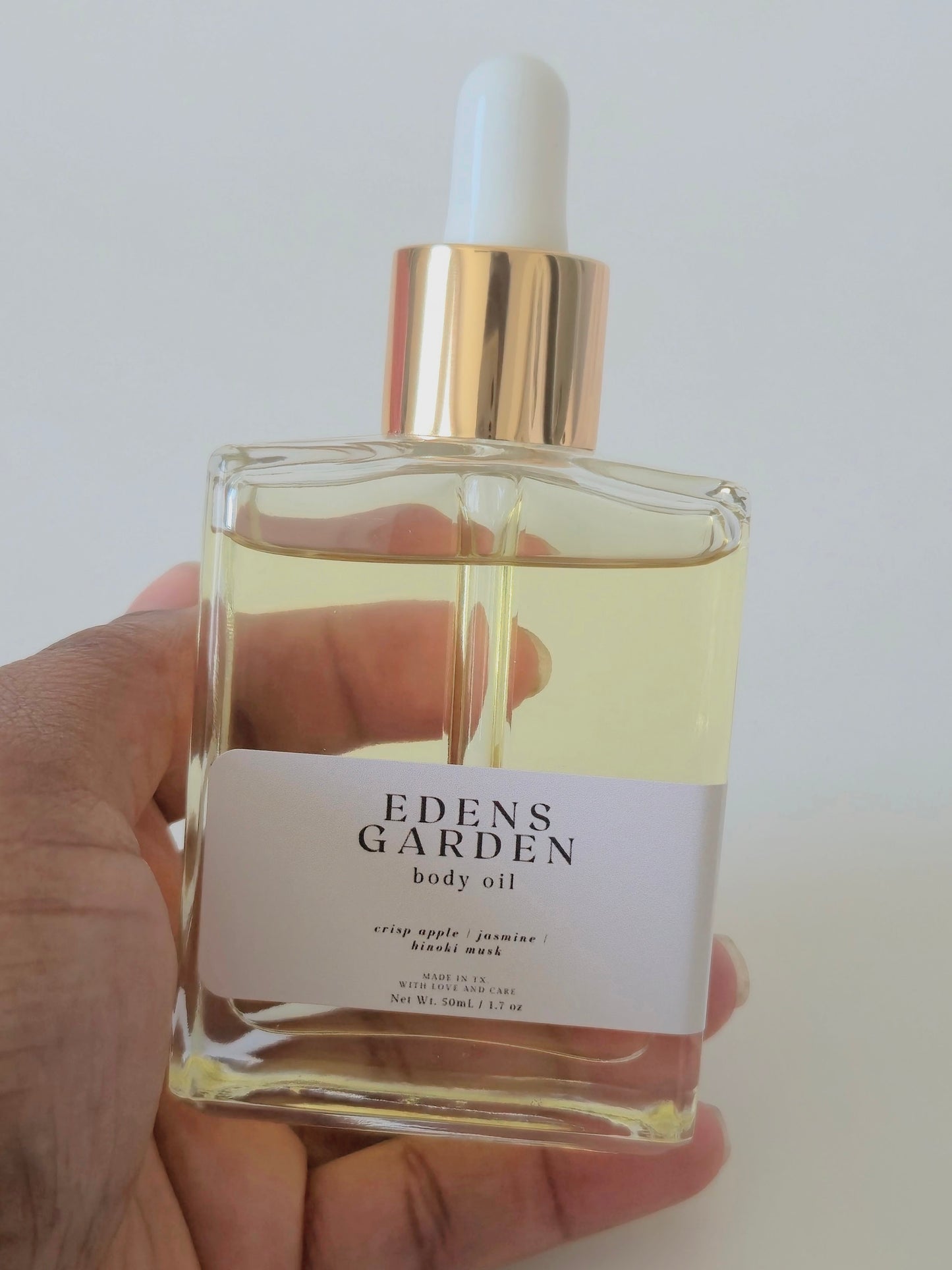 Eden's Garden body oil bottle held in a hand against a plain background