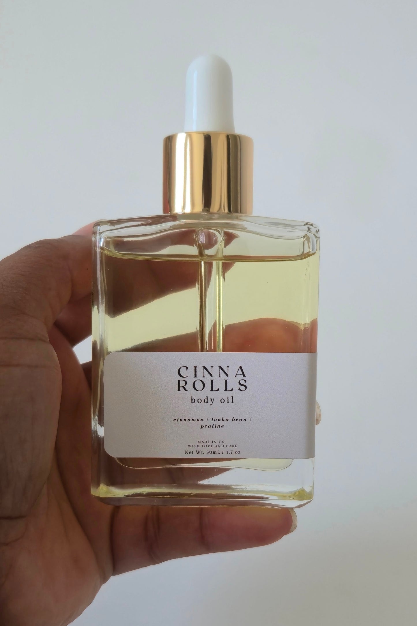 Cinna Rolls body oil bottle held by a hand against a white background