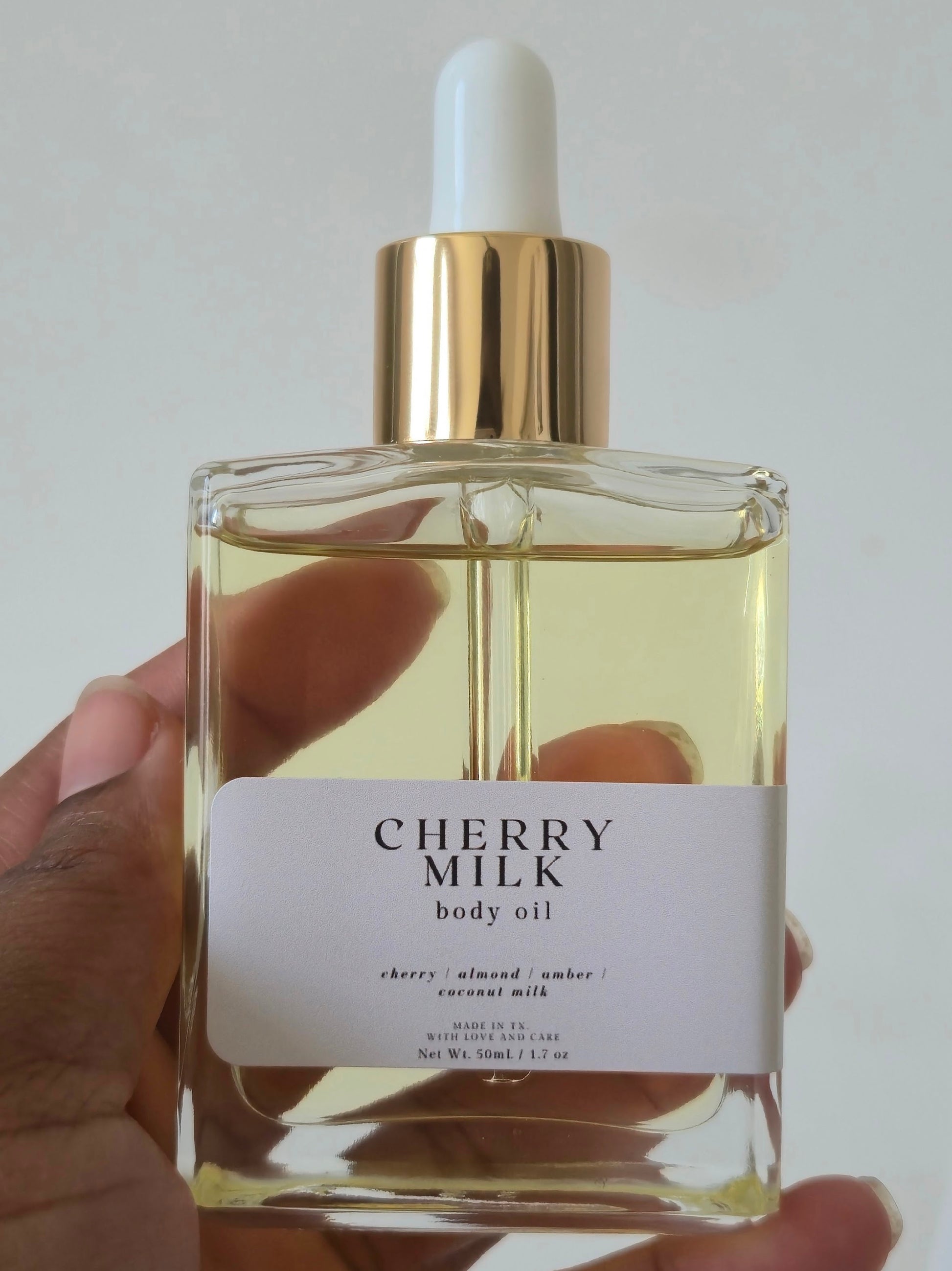 Bottle of Cherry Milk body oil held by a hand against a white background