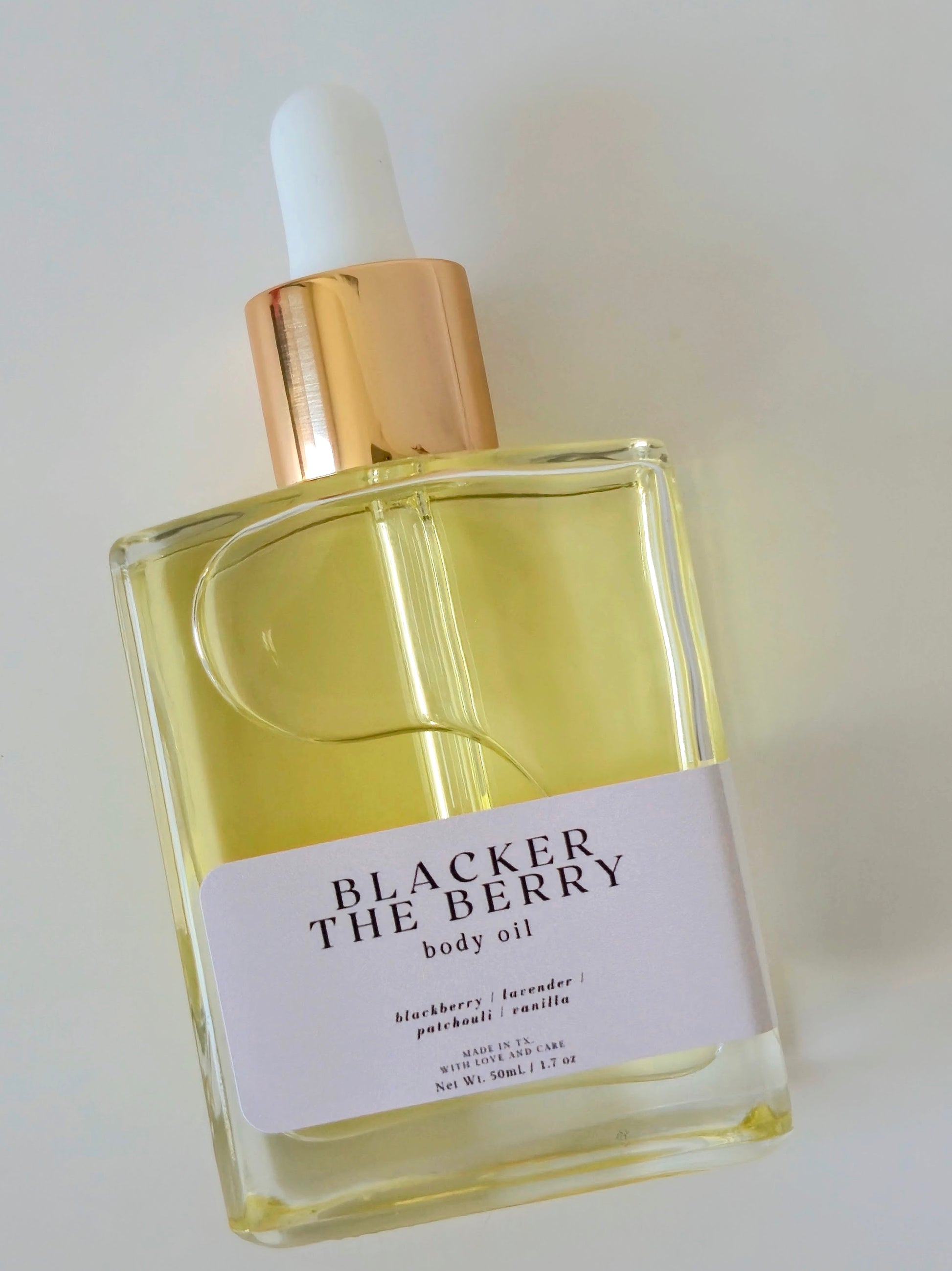 Bottle of Blacker The Berry body oil with a gold cap on a light background