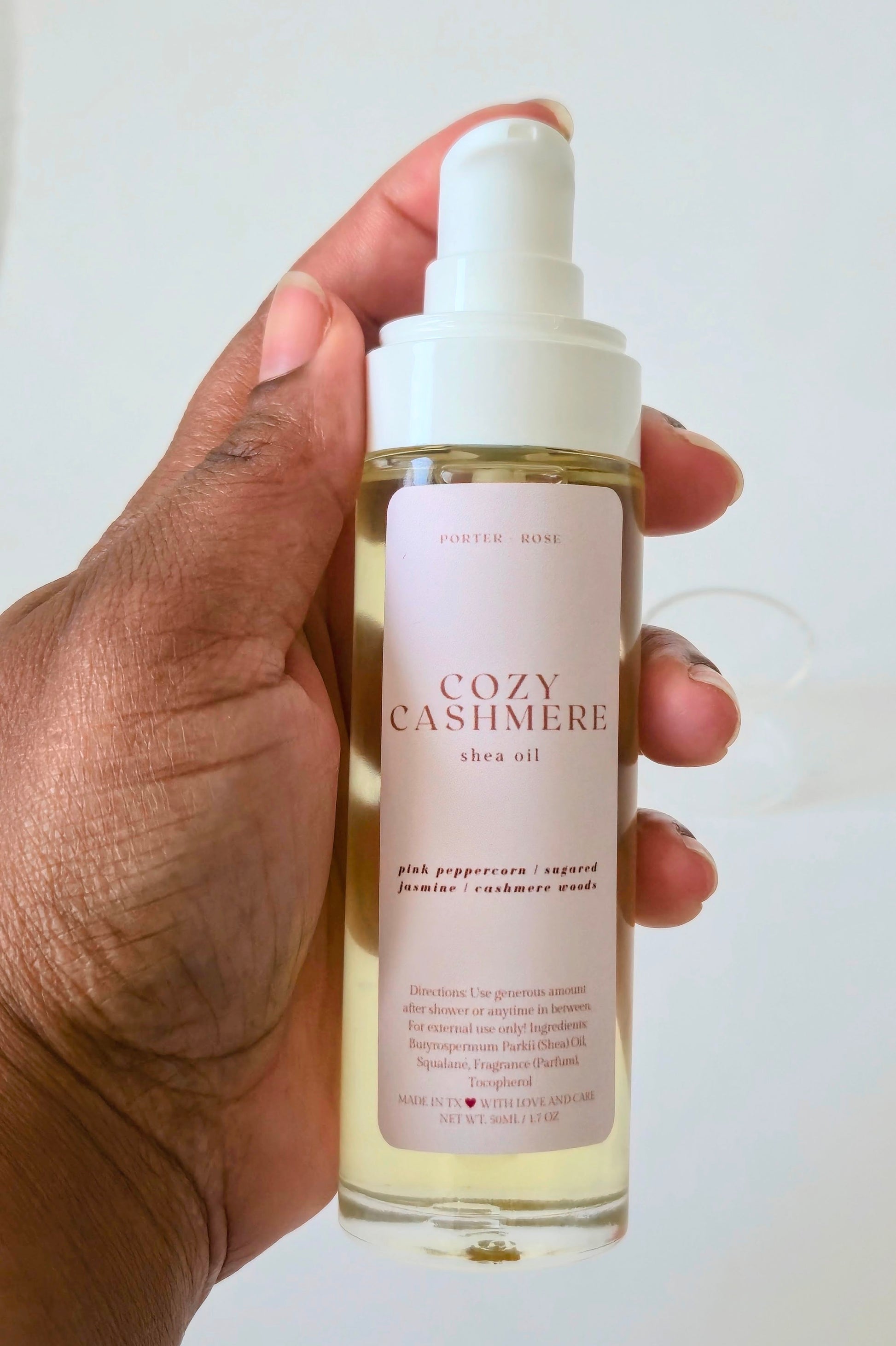 Hand holding a bottle of Cozy Cashmere shea oil against a white background