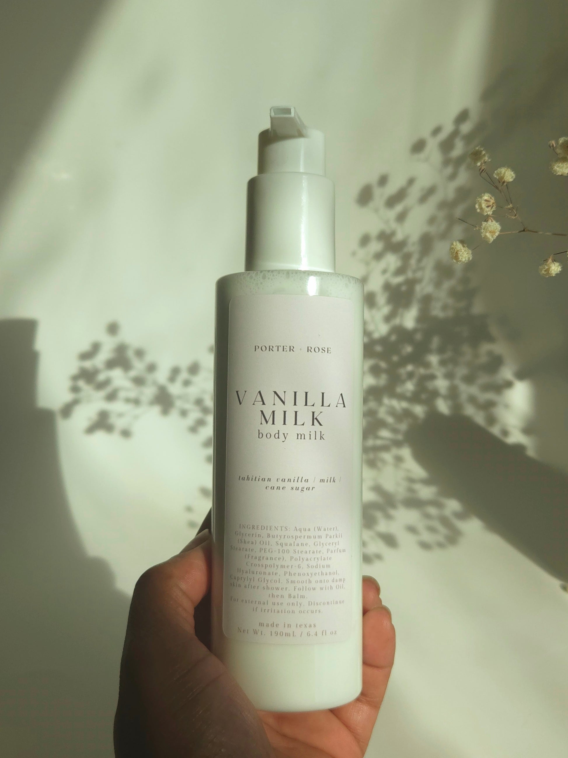 Hand holding a bottle of Vanilla Milk body milk against a neutral background