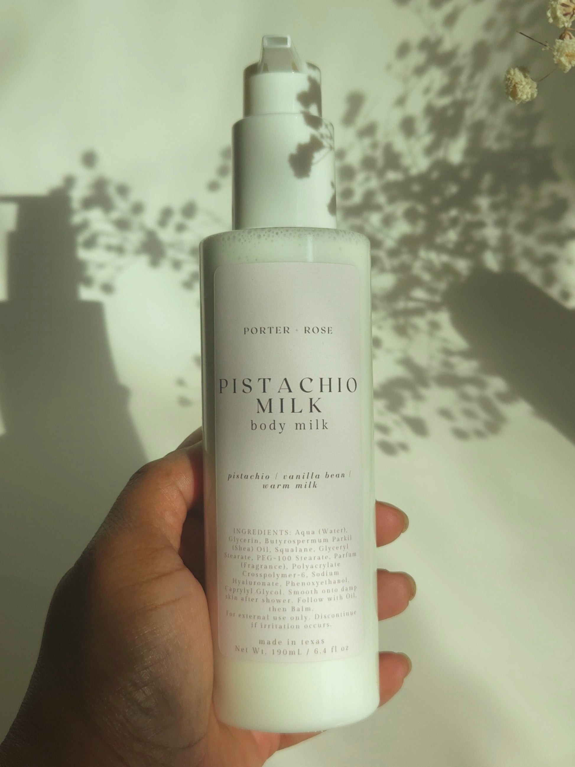 Hand holding a bottle of Pistachio Milk body milk with a light background