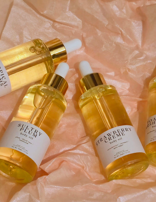 Three bottles of Sultry Plum and Strawbery Creme body oils on a soft pink background.