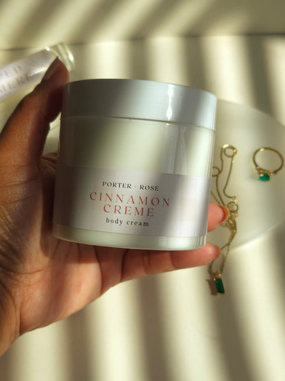 Hand holding a jar of 'Cinnamon Crème' body cream with a blurred background