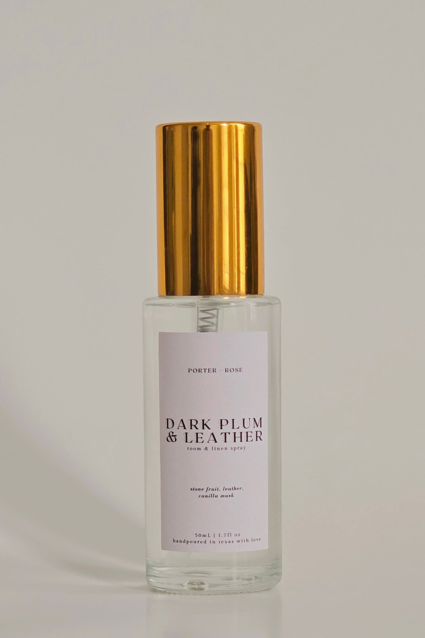 Perfume bottle labeled 'Dark Plum & Leather' with gold cap on a light gray background