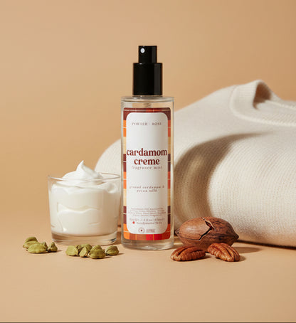 A bottle of Porter Rose Cardamom Creme Fragrance Mist with a black spray pump and a white label featuring orange and brown accents, set against a neutral light gray background.