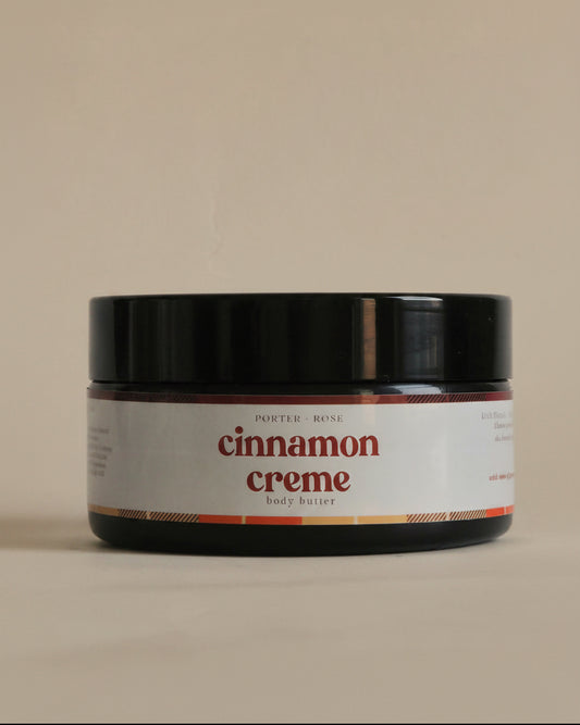 A black cosmetic jar of 'cinnamon creme' by 'porter rose' with a white label, shown against a plain light gray background.