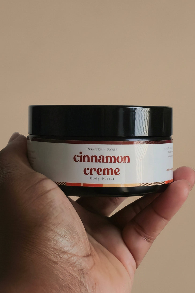 A hand holding a small jar of cinnamon creme against a plain light gray background.