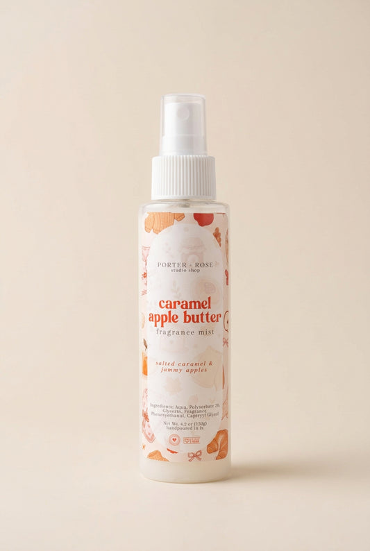 A bottle of Porter Rose Caramel Apple Butter fragrance mist with a white spray top and a label decorated with orange and peach illustrations, set against a white background with soft diagonal shadows.