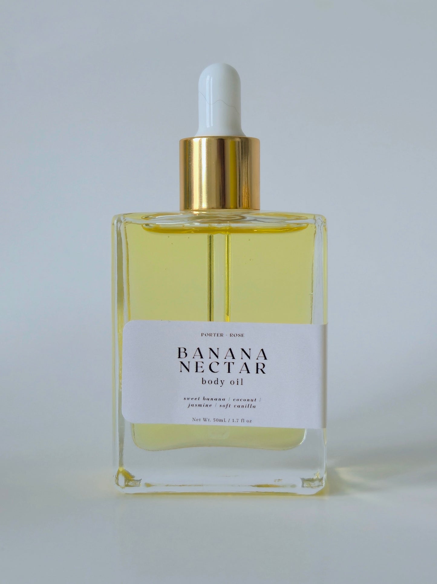 Bottle of Banana Nectar body oil with a white label on a light gray background