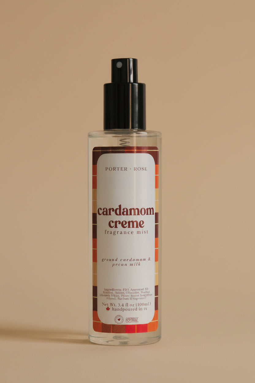 A bottle of Porter Rose Cardamom Creme Fragrance Mist with a black spray pump and a white label featuring orange and brown accents, set against a neutral light gray background.