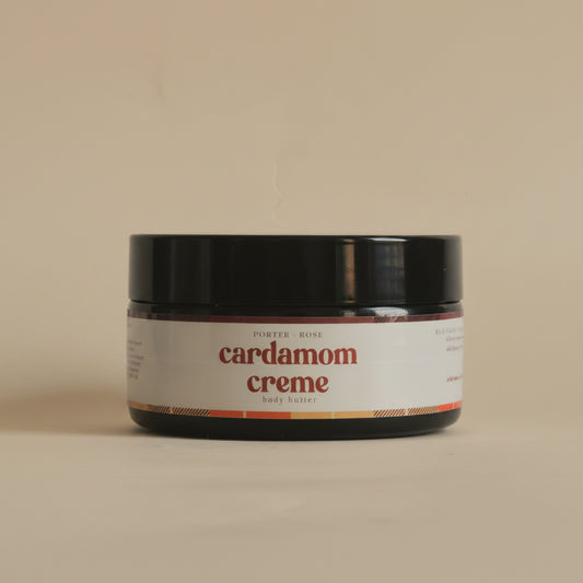 A black cosmetic jar of 'cardamom creme' by 'Porter + rose ' with a white label, shown against a plain light gray background.