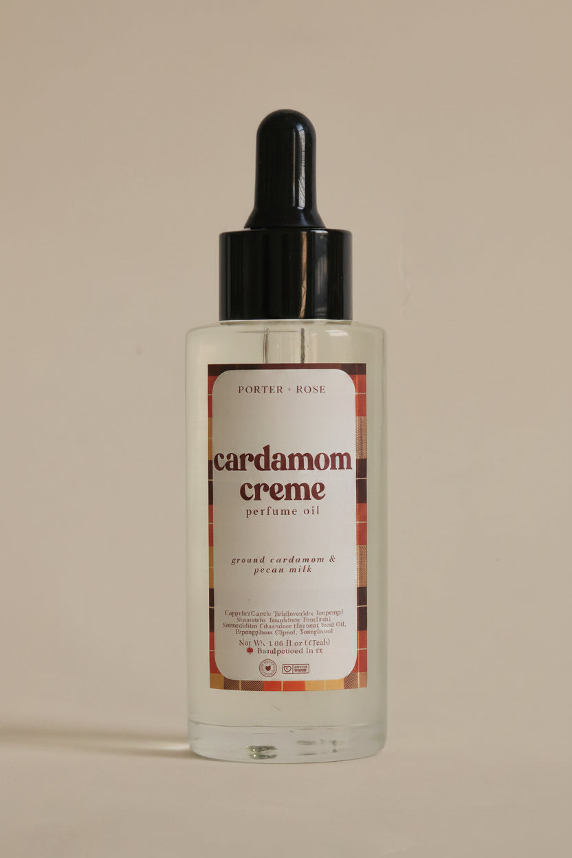 A clear bottle of Porter Rose Cardamom Creme perfume oil with a black dropper cap and a cream-colored label, set against a plain light gray background.