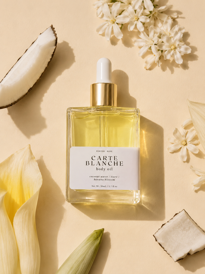 Carte Blanche body oil bottle with flowers and coconut on a beige background