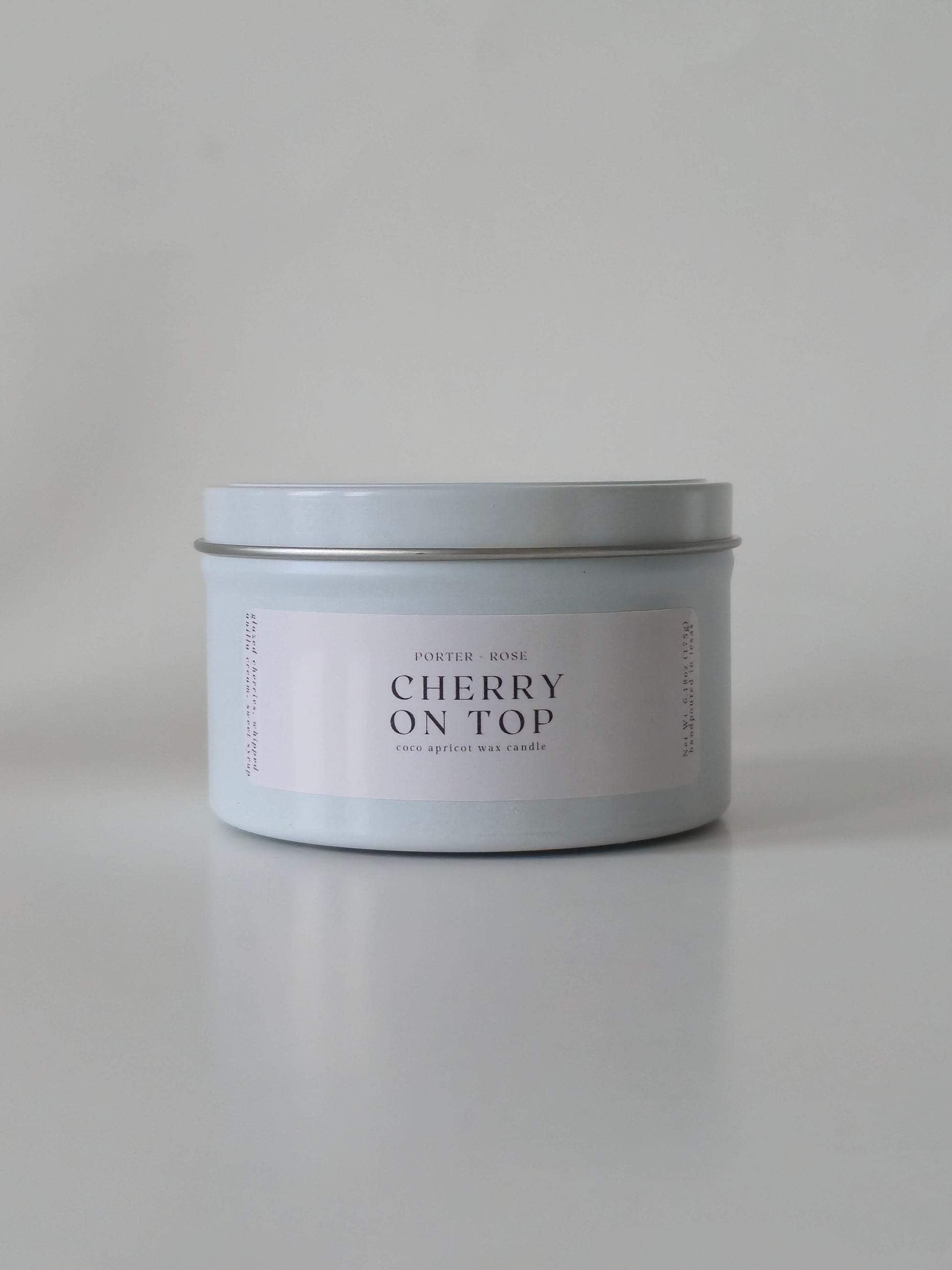 Candle in a silver tin labeled 'Cherry on Top' on a light gray background