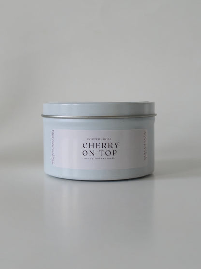Candle in a silver tin labeled 'Cherry on Top' on a light gray background