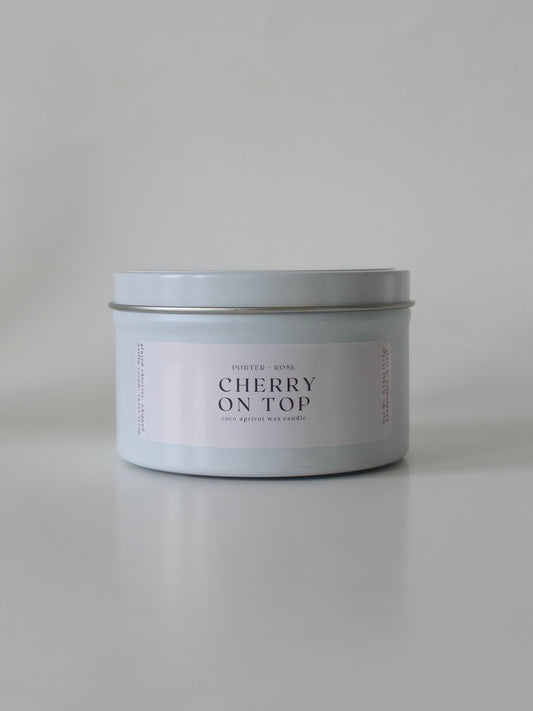 Candle in a silver tin labeled 'Cherry on Top' on a light gray background