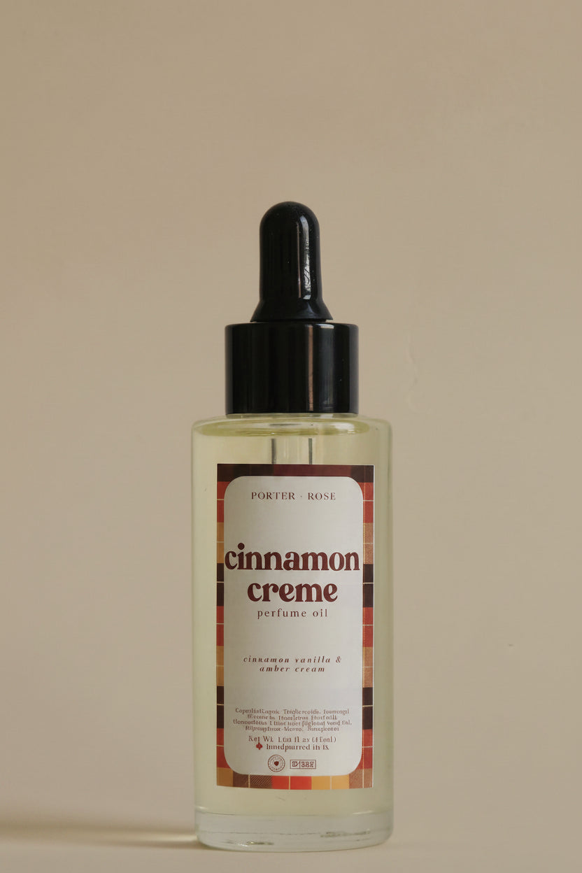 A clear glass bottle of porter rose Cinnamon Creme body oil with a black dropper cap, shown against a plain light gray background.