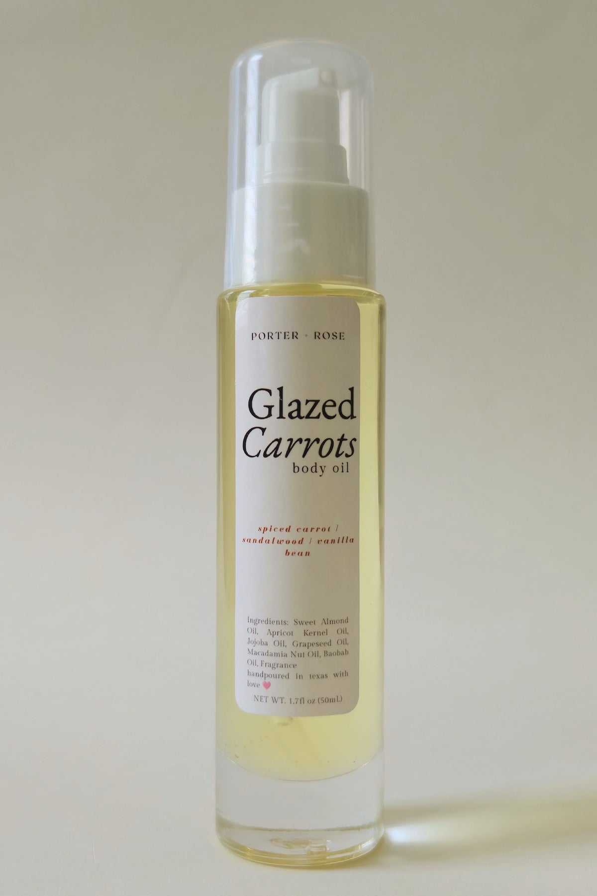 A bottle of Porter & Rosé Glazed Carrots body oil with a clear cap and white label, showing the pale yellow oil inside, set against a plain light beige background.