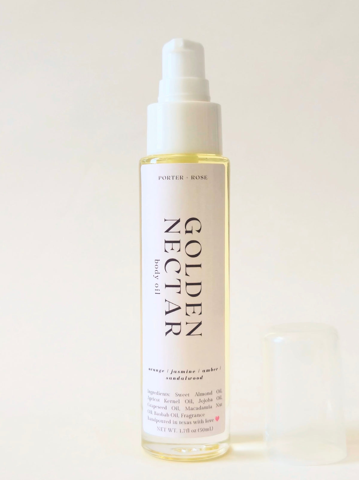 A bottle of Porter Rose Golden Nectar body oil with a white pump dispenser and a small clear cap placed beside it on a light beige background.