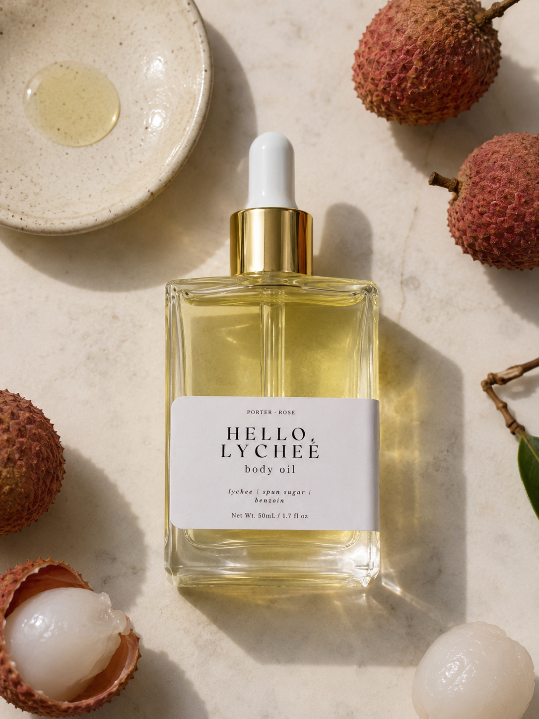 Body oil bottle labeled 'Hello Lychee' with lychees around on a neutral background