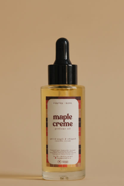 A clear bottle of perfume oil with a black dropper cap and a white label reading 'maple creme' on a light gray background.