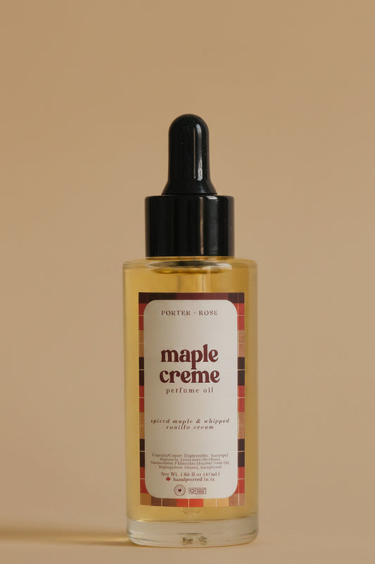 A clear bottle of perfume oil with a black dropper cap and a white label reading 'maple creme' on a light gray background.