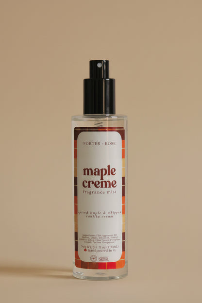A clear cylindrical bottle of Porter's Rose Maple Creme body mist with a black spray nozzle, shown on a light gray background with its black cap placed below it.
