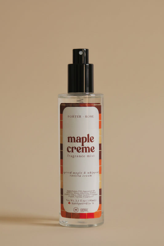 A clear cylindrical bottle of Porter's Rose Maple Creme body mist with a black spray nozzle, shown on a light gray background with its black cap placed below it.