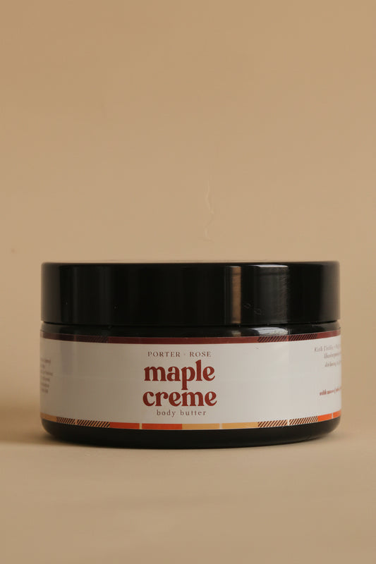 A black plastic jar of maple creme body butter with a white label, shown against a plain light gray background.