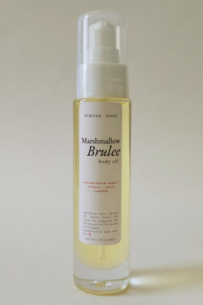 A bottle of Porter Rose Marshmallow Brulee body oil, featuring a clear glass bottle with a white pump dispenser and a white label, set against a plain light beige background.