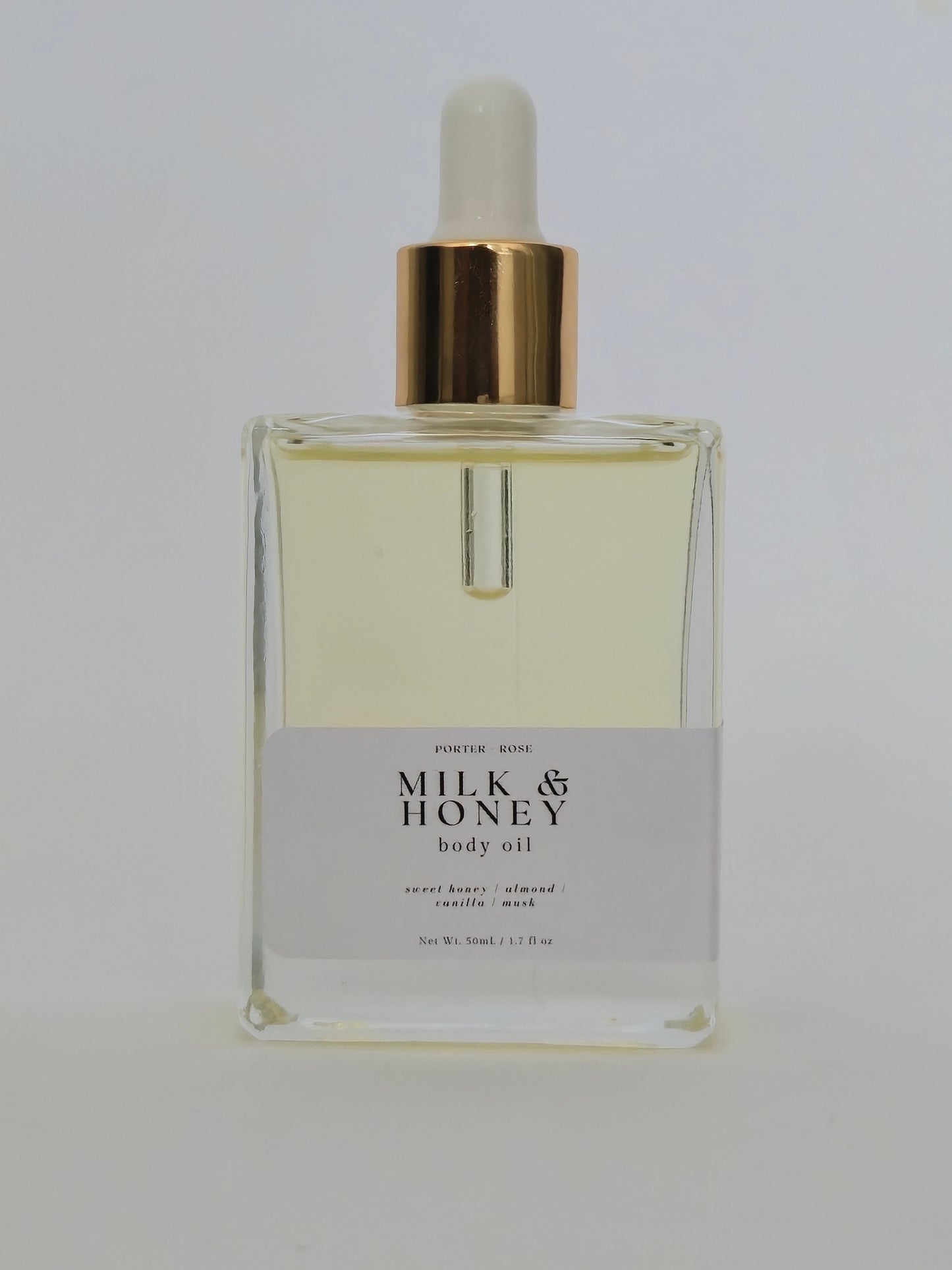 A rectangular glass bottle of Milk & Honey Body Oil with a white label and a gold collar, featuring a white dropper cap, set against a plain white background.
