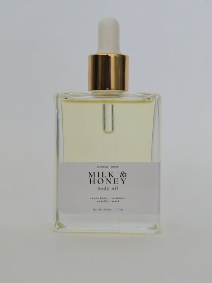 A rectangular glass bottle of Milk & Honey Body Oil with a white label and a gold collar, featuring a white dropper cap, set against a plain white background.