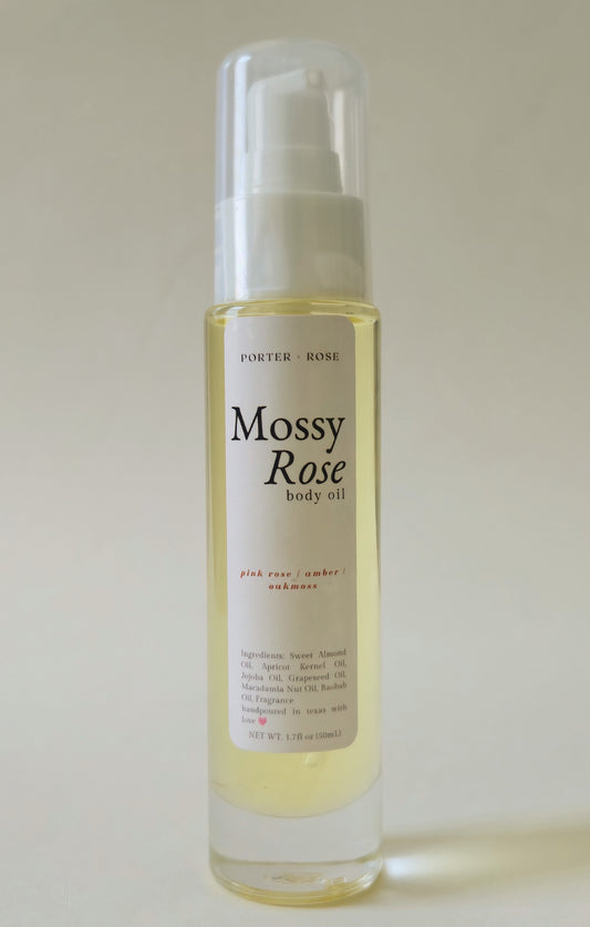 A bottle of Porter Rose Mossy Rose body oil with a white pump dispenser and clear cap, containing a pale yellow liquid, set against a plain light beige background.