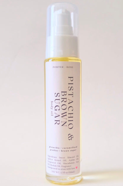 A clear glass pump bottle of Pistachio & Brown Sugar body oil with a white label, set against a plain off-white background.