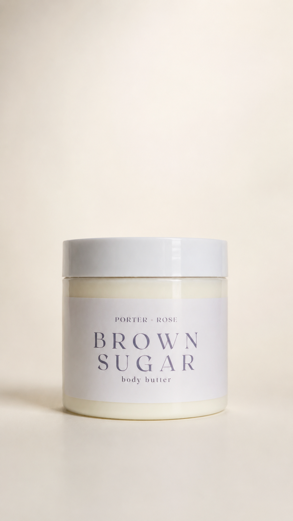 A jar of porter ROSE Brown Sugar body butter, featuring a white label with dark gray text and a matching white lid, set against a warm cream background.